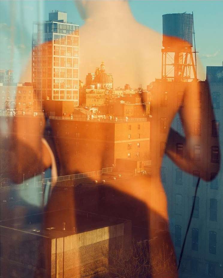 Back of an adult with transparent overlay of urban buildings including rooftops, water towers, and brick apartment buildings on sunny day.