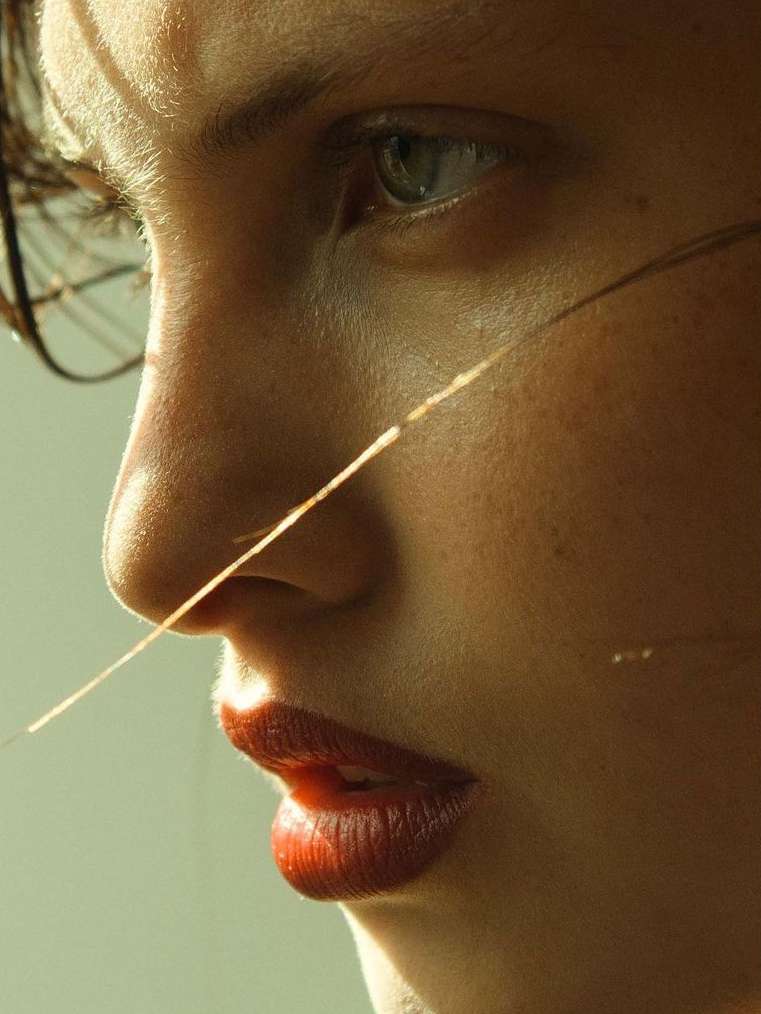 Close-up portrait of a woman with red lipstick and natural skin texture, softly lit with focus on facial features and minimalistic style.
