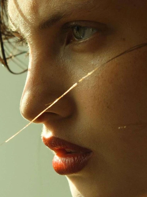 Close-up portrait of a woman with red lipstick and natural skin texture, softly lit with focus on facial features and minimalistic style.