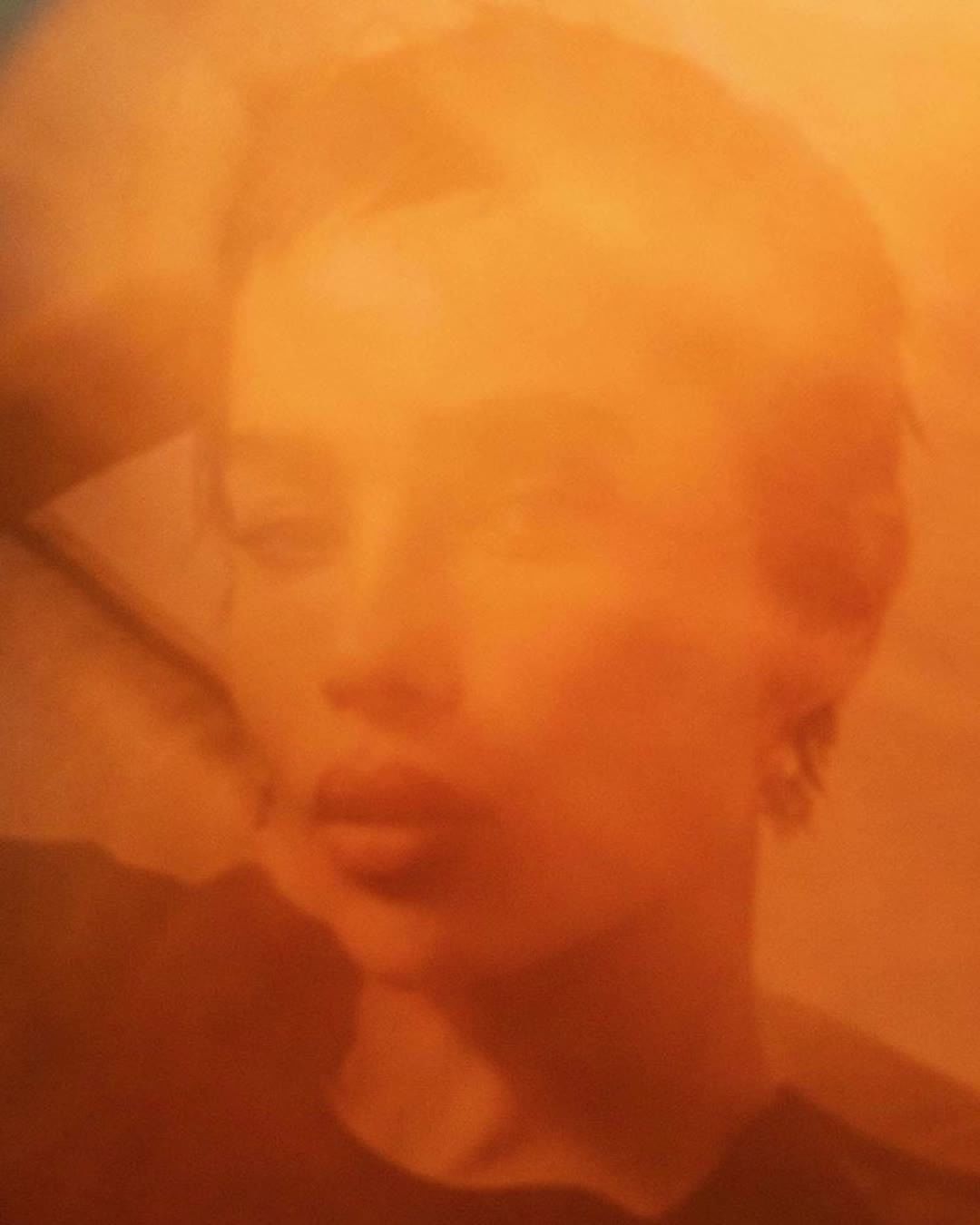 Portrait of a woman with short hair in warm tones, featuring soft focus and shallow depth of field in an indoor setting.