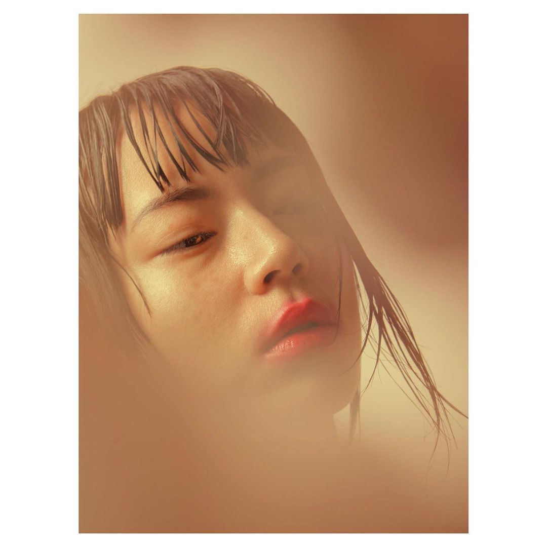 Close-up portrait of a woman with wet hair and glossy red lips against warm amber tones.