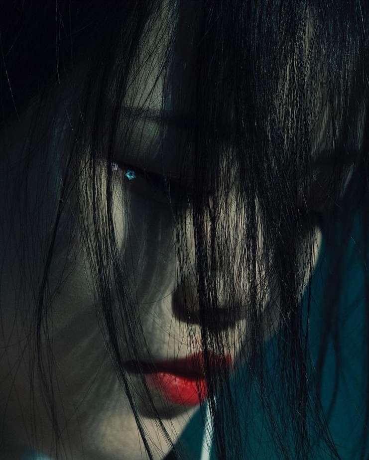 Close-up studio portrait of a young adult woman with long black hair and red lipstick in dramatic lighting.
