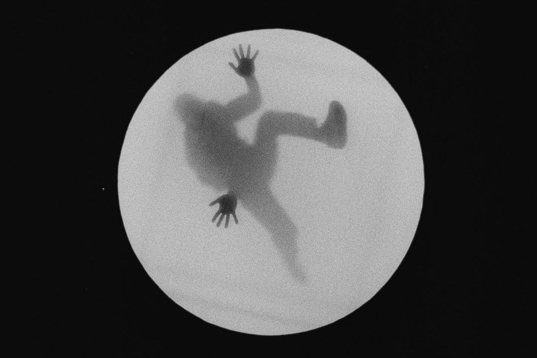 Silhouetted figure reaching in white circle against black, high angle. Monochrome image shows motion and disorientation.