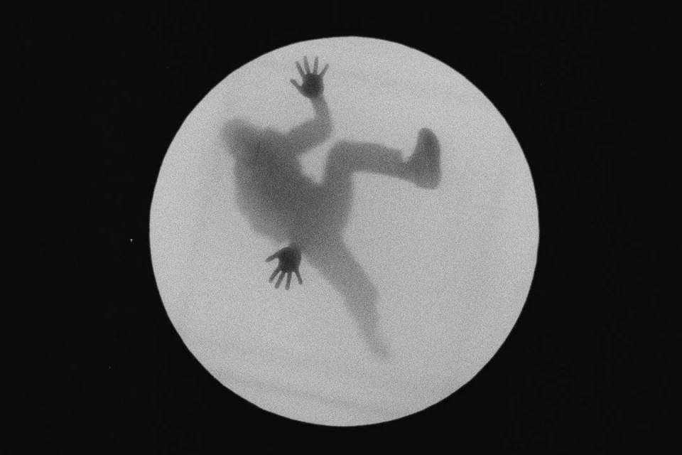Silhouetted figure reaching in white circle against black, high angle. Monochrome image shows motion and disorientation.