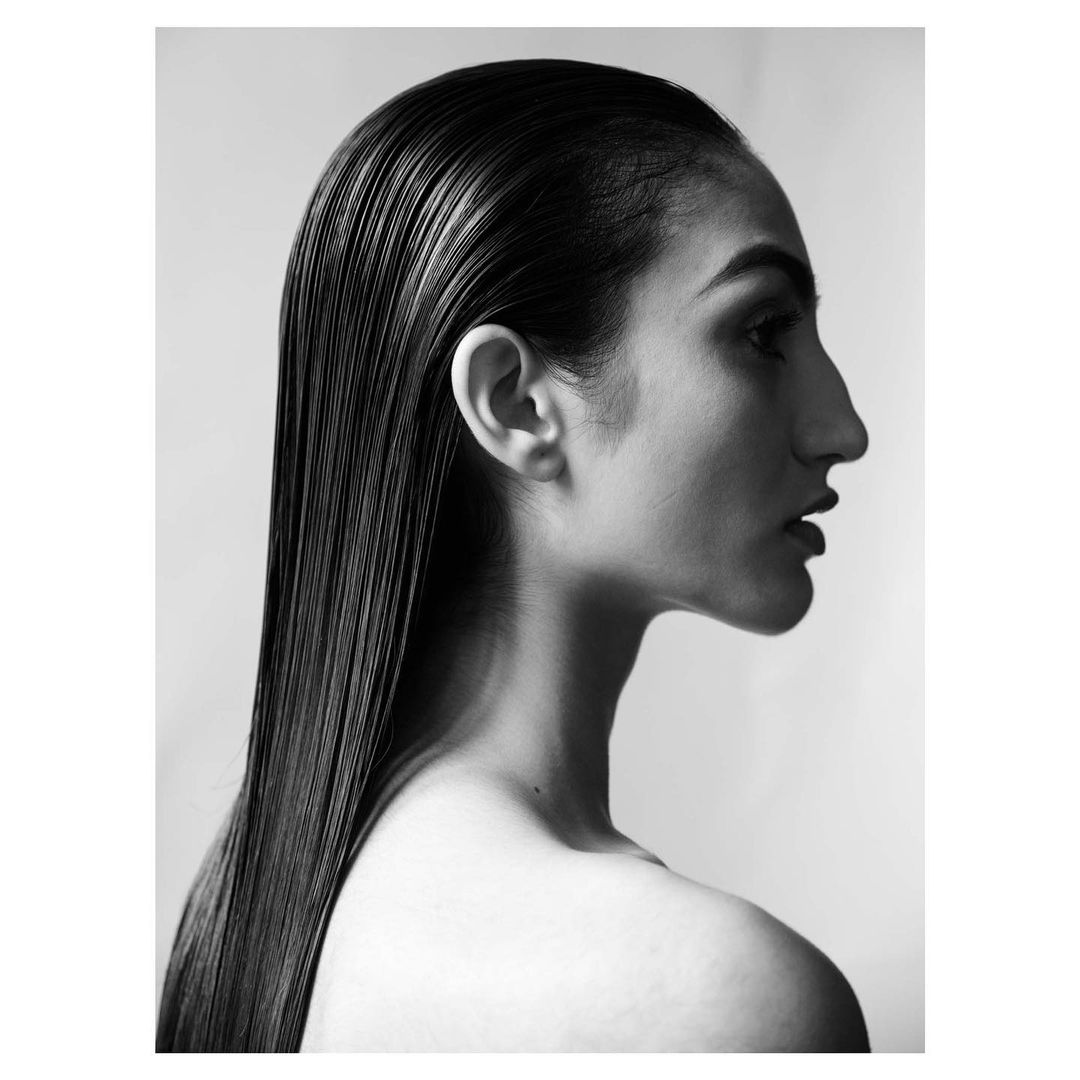 Monochrome portrait of an adult female in profile, featuring sleek, dark hair and clean beauty lighting against a neutral background.