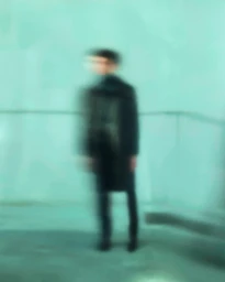 Motion blurred portrait of a person standing against a turquoise background by Christopher Anderson