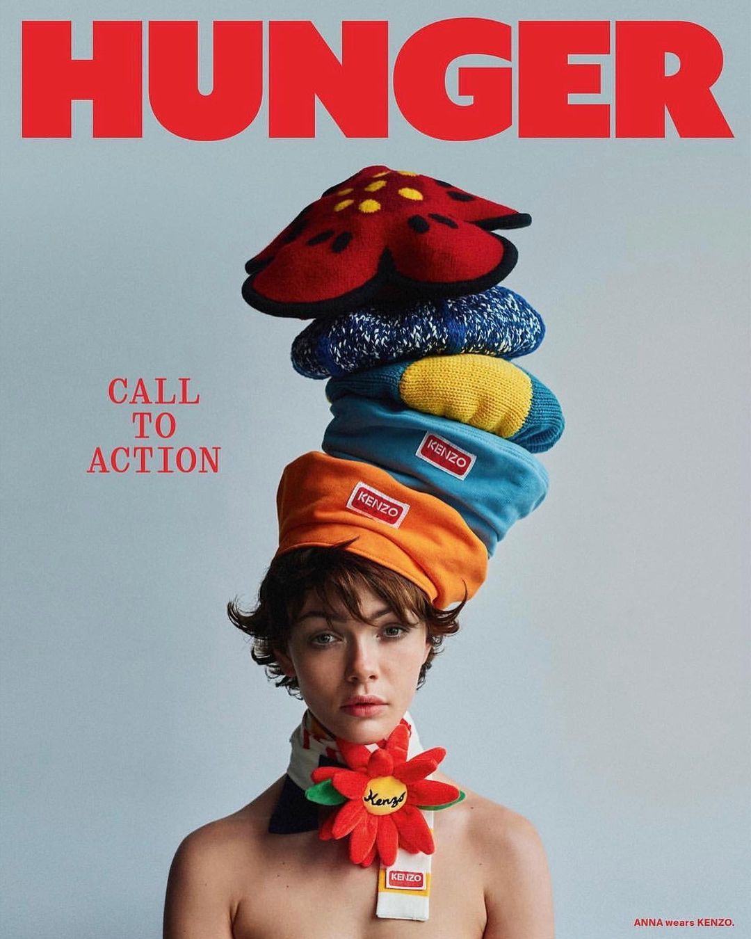 Brunette woman poses wearing multiple knit hats and scarf with KENZO logo. Red HUNGER magazine logo is at the top of the magazine cover.
