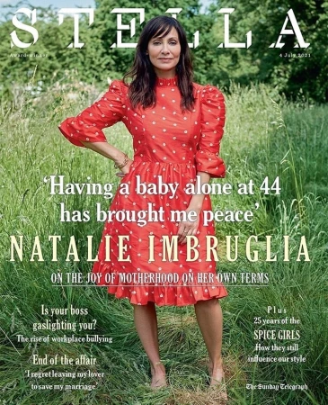 Natalie Imbruglia standing in a lush green meadow wearing a red patterned dress for a magazine cover portrait.