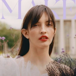 Close-up portrait of a woman with dark hair and red lipstick wearing a sheer polka-dot tulle dress outdoors.