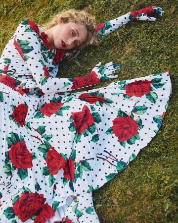 Model lying on grass wearing a white dress and matching gloves patterned with black polka dots and red roses