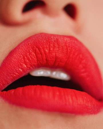Extreme macro close-up of vibrant red matte lipstick on parted lips revealing white teeth by Christopher Fenner.