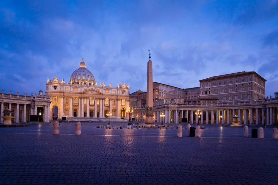 St. Peter's Basilica and Square in Vatican City at dusk, featuring the iconic dome, obelisk, colonnades, and cobblestone piazza.