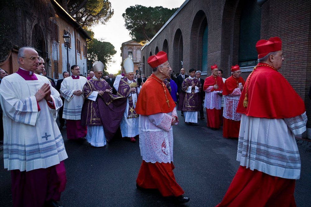 Procession of cardinals and clergy walking in Rome, Italy, wearing traditional religious attire, including red robes and hats.