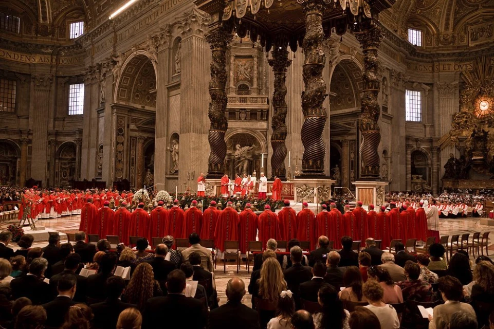 Interior view of St. Peter's Basilica with a large group of religious figures in red robes and a seated audience, all in a sepia tone.
