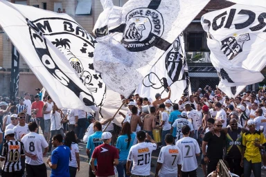 Large crowd of football fans waving large white and black team flags outdoors in a street