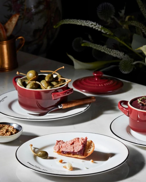 Overhead shot of appetizers featuring pate on toast, capers, and small bowls of food on a white marble surface with floral background.