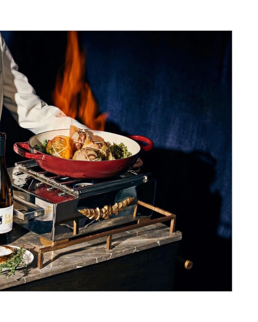 Overhead food presentation featuring a red pot on a warmer with a side of wine, offering a rustic, gourmet dining experience indoors.