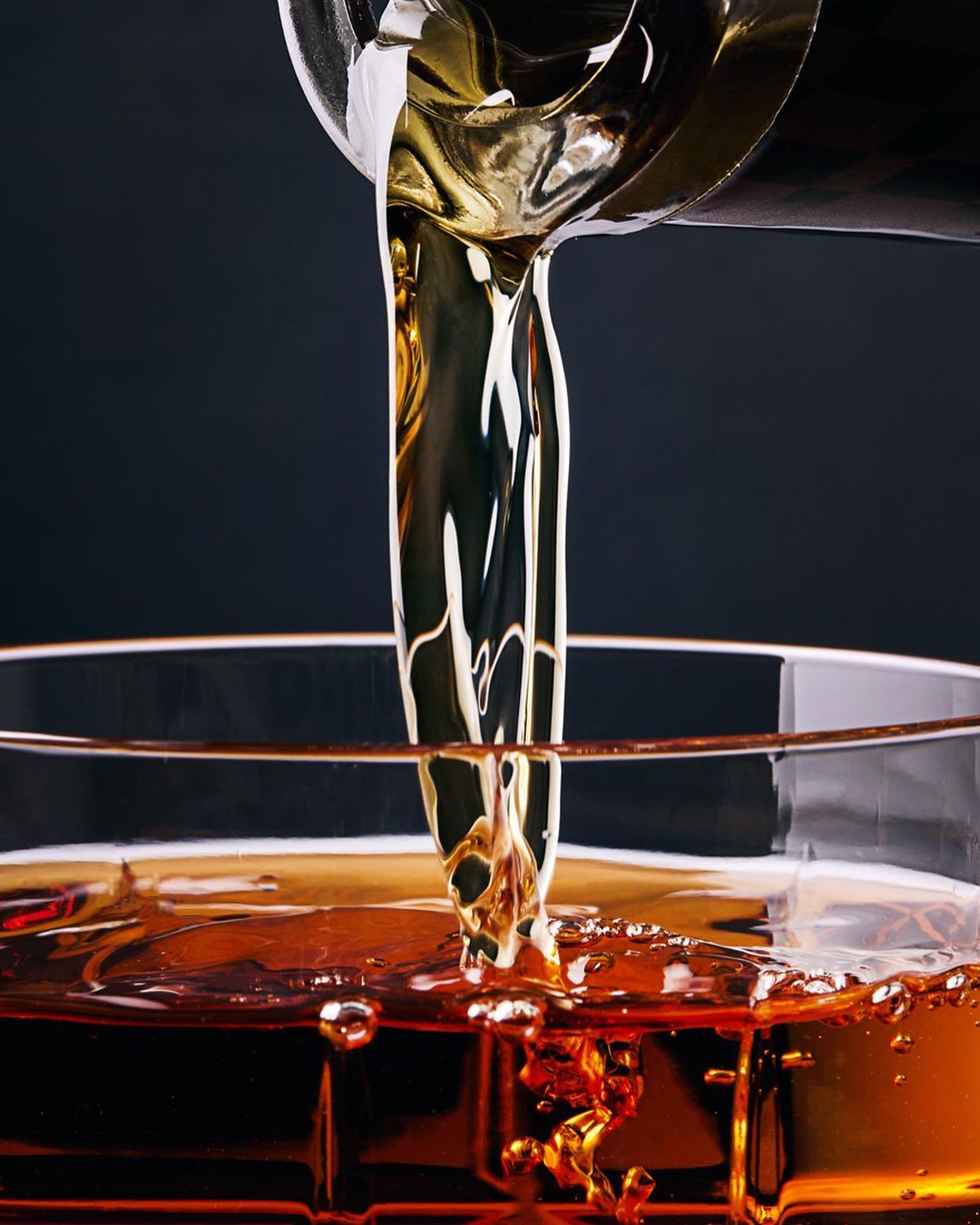 Close-up shot of amber liquid being poured into a glass, showcasing the fluid dynamics and color, with a dark background.