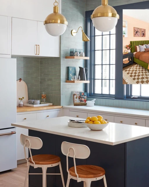 Bright, modern kitchen interior featuring white cabinets, a navy island with lemons, and two stools. Natural light streams through a window.