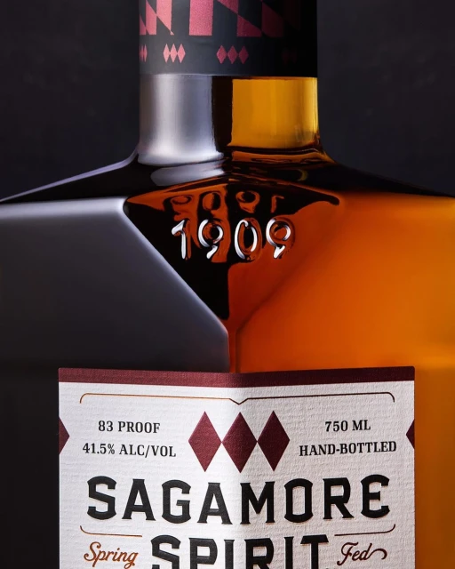 Close-up of a bottle of Sagamore Spirit, highlighting the brand name, 1909 embossing, and details on the label against a dark background.