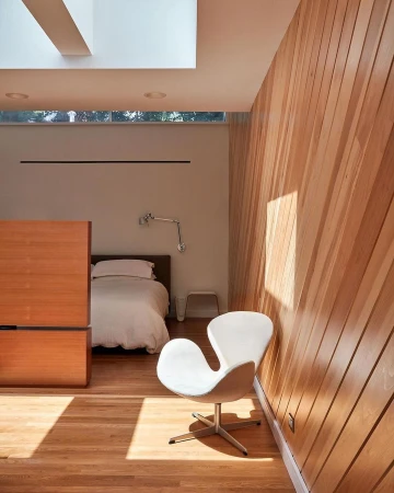 Swan chair in a bedroom with wood-paneled wall and hardwood floor illuminated by sunlight. Bed and skylight visible.