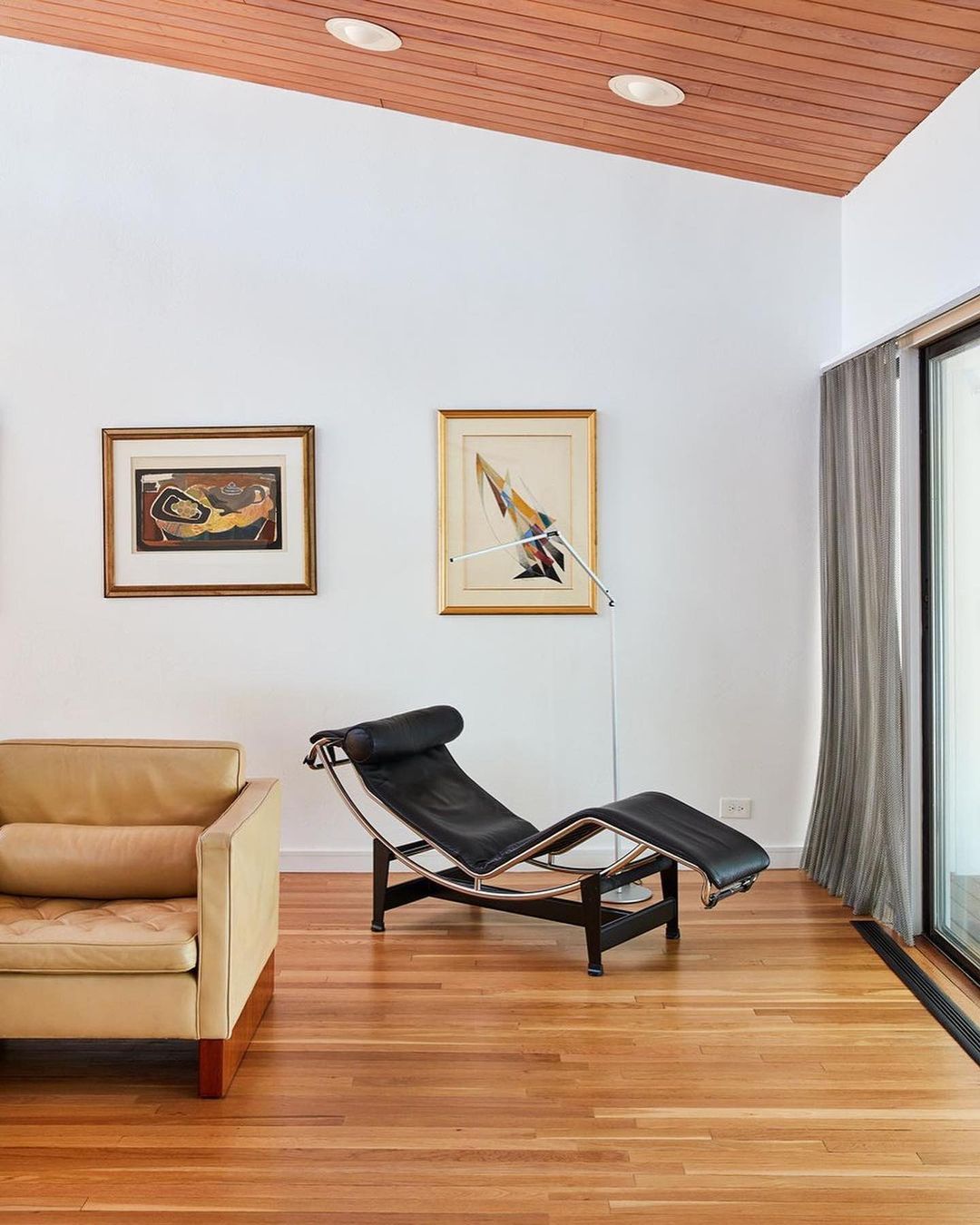 Interior view featuring a black chaise lounge, tan sofa, framed wall art, hardwood floors, and a wood-paneled ceiling with recessed lights.