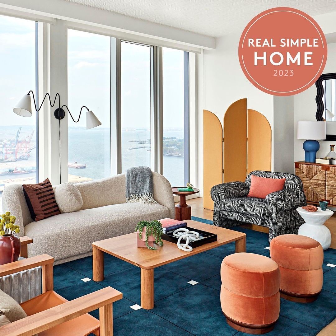 Contemporary living room interior featuring a cream couch, geometric rug, wooden furniture, and natural light from large windows.