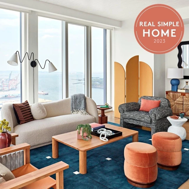Contemporary living room interior featuring a cream couch, geometric rug, wooden furniture, and natural light from large windows.
