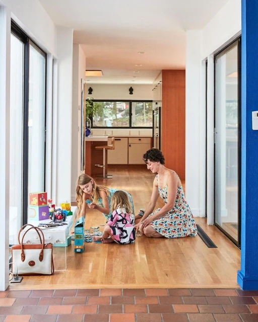 Mother and two daughters assembling a jigsaw puzzle on a wooden floor in a modern home with natural light and playful atmosphere.