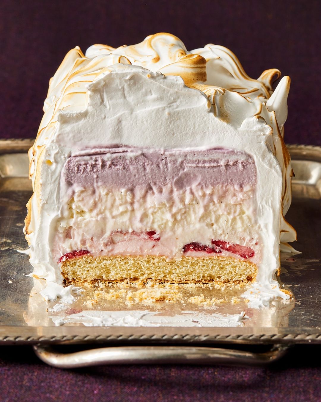 Close-up studio shot of a multi-layered baked Alaska cake dessert, showcasing its sponge cake, cream, ice cream, and torched meringue layers.