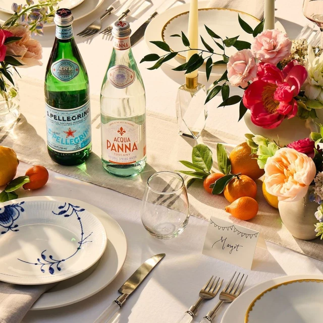 Elegant table setting with water bottles, flower arrangements, and place settings featuring fine china and silverware.