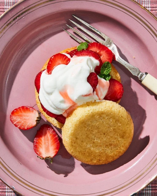 Overhead shot of strawberry shortcake dessert with fresh strawberries, whipped cream, and mint sprigs on a pink plate with a fork.