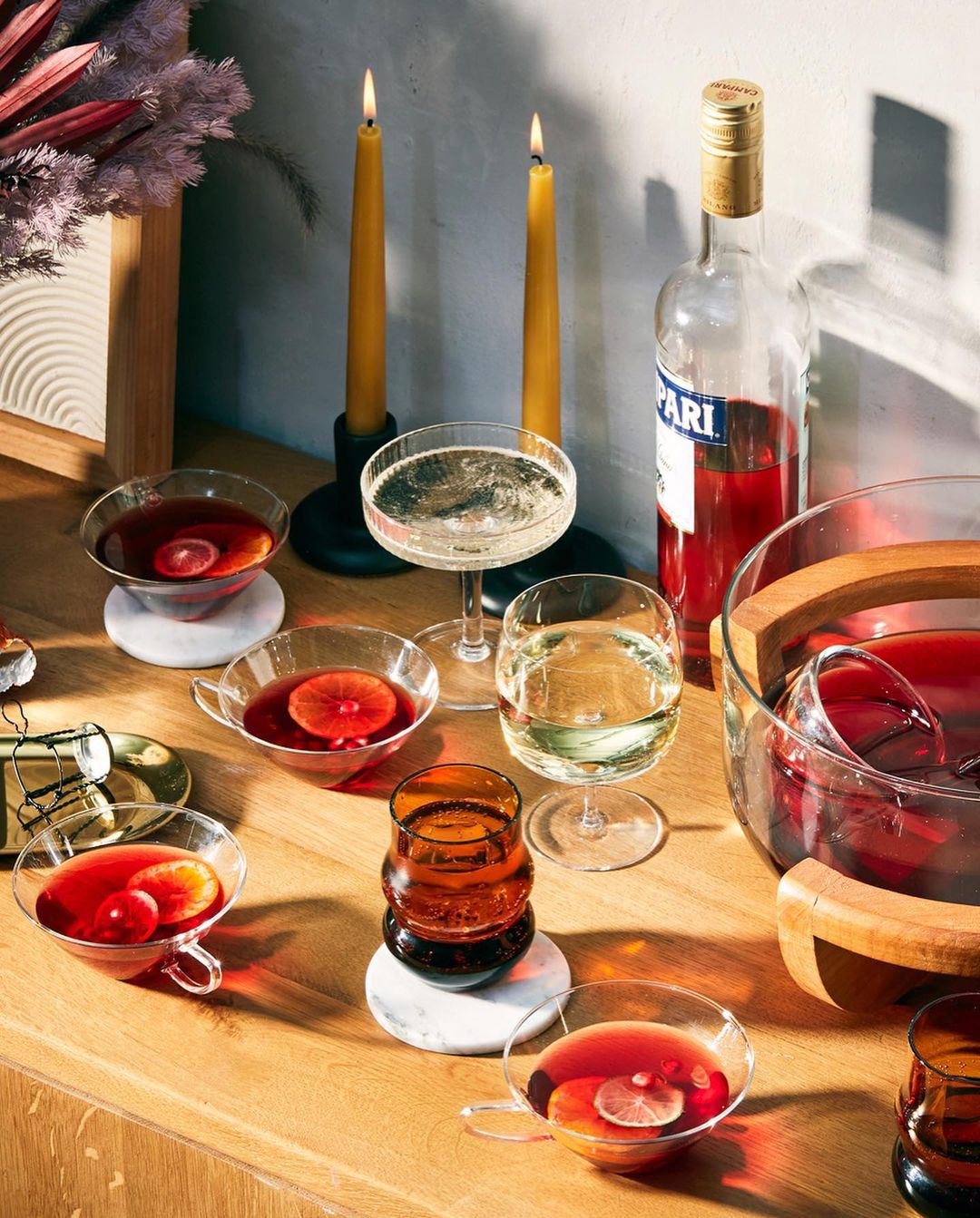 Festive gathering featuring an assortment of cocktails and beverages, including wine and a punch bowl, arranged on a wooden table top.
