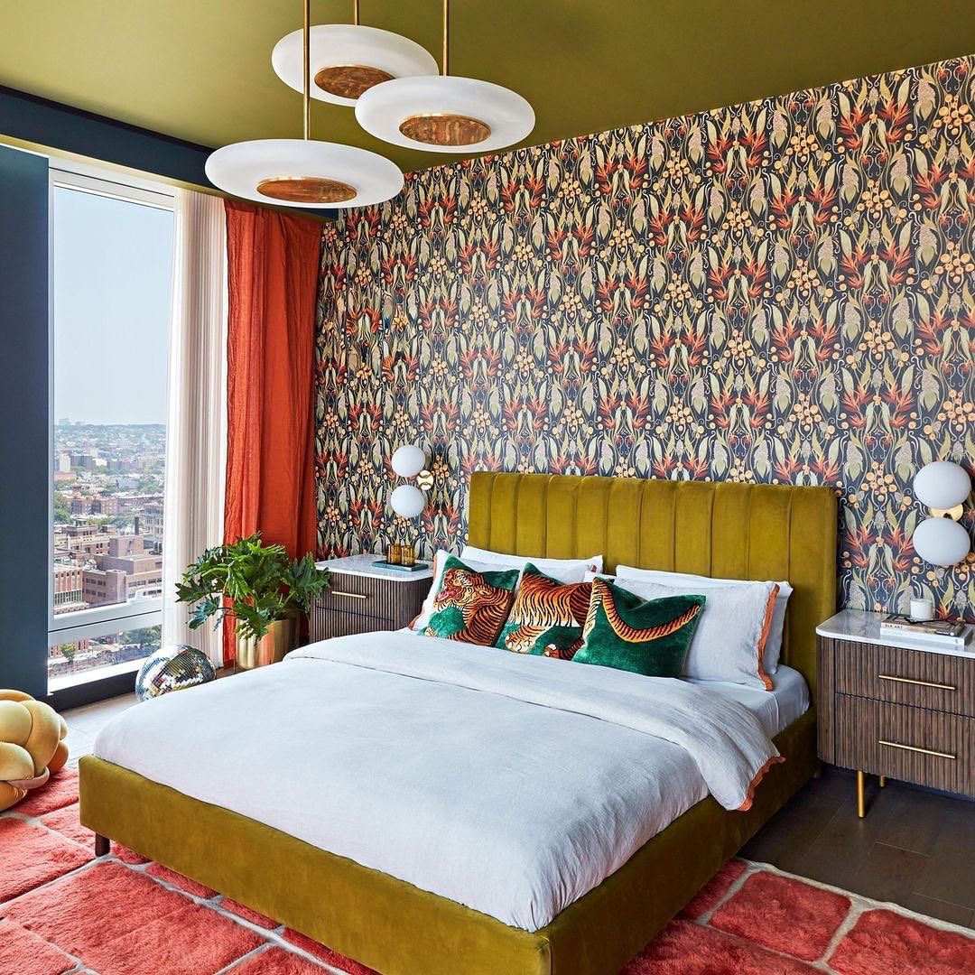 Bedroom interior with a large bed, patterned wallpaper, and city view through a window, featuring a blend of contemporary and art deco style.