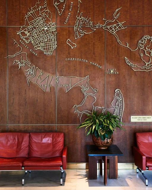 Interior view featuring a wooden wall with a map design, red leather sofas, a potted plant on a table, and minimalist decor in a waiting area.