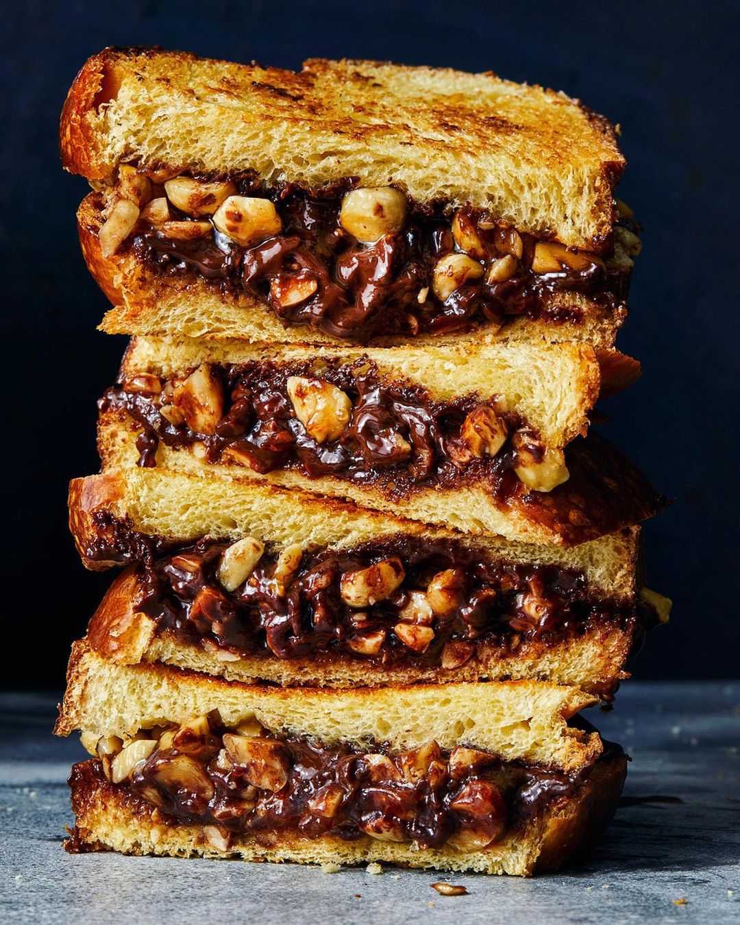 Stacked sandwich halves filled with nuts and chocolate, set against a dark background, showcase a delicious food presentation.