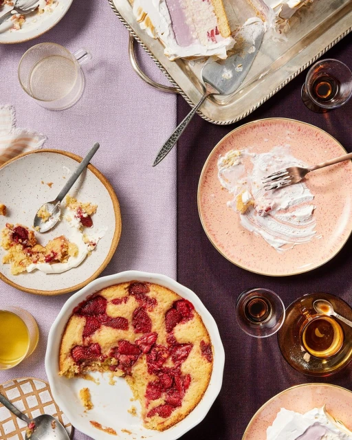 Overhead shot of dessert cakes and pies served on plates and trays, accompanied by glasses of liquor on a two-tone tablecloth.