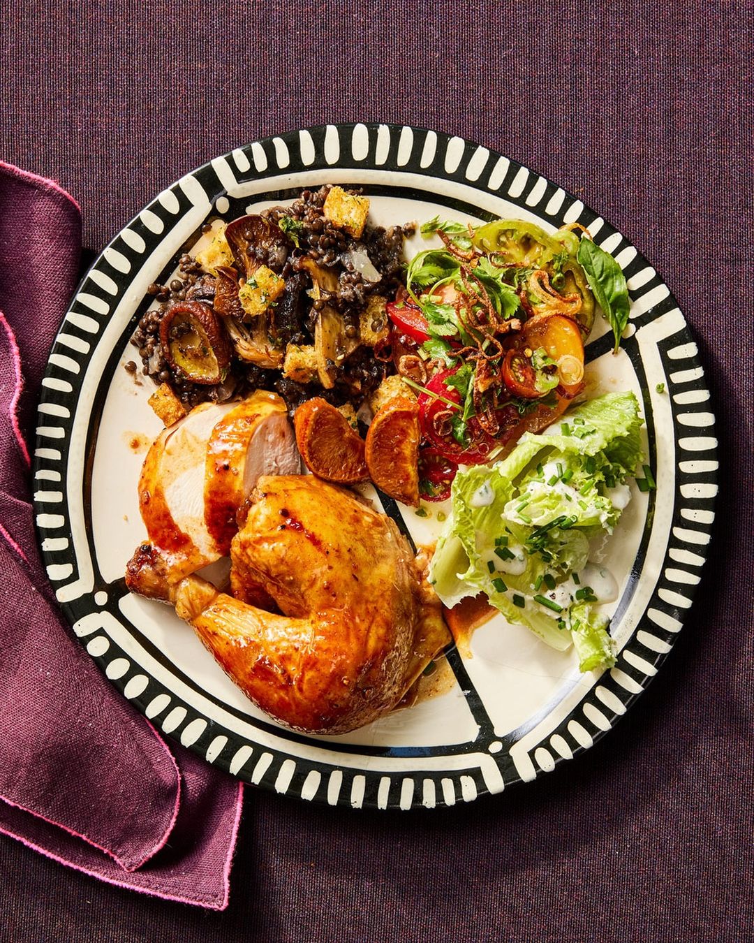 Overhead shot showcases roasted chicken quarter, lentil salad with toasted bread, and green salad on an ornate white plate.