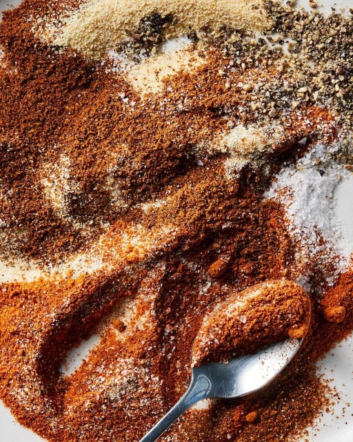 Overhead shot of various spices and seasonings, including paprika, salt, pepper, and other powders, with a spoon dusted with spices.