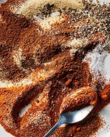 Overhead shot of various spices and seasonings, including paprika, salt, pepper, and other powders, with a spoon dusted with spices.