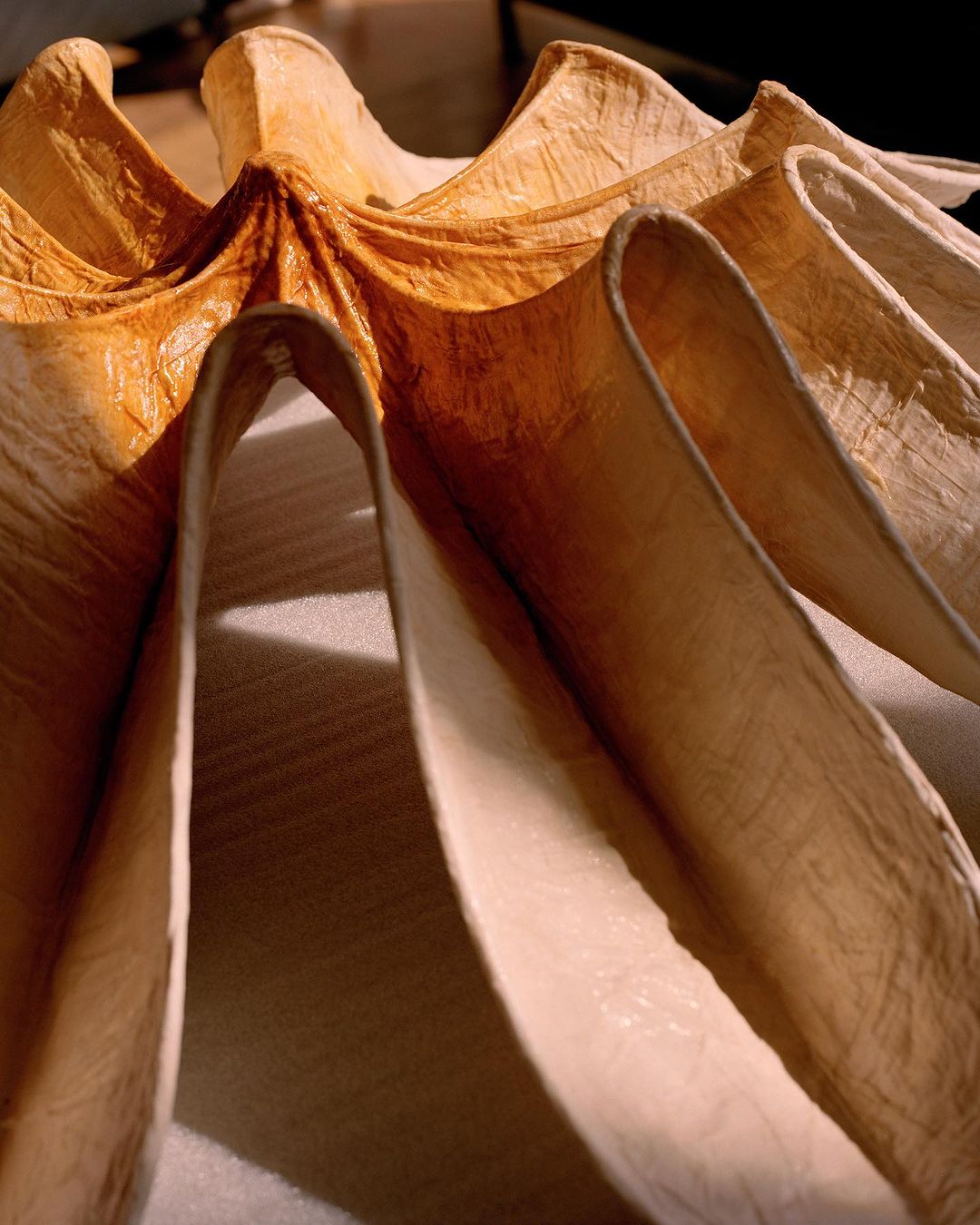 Textured cream and light brown paper art piece with layered, folded patterns, showcasing depth and organic design in a studio setting.