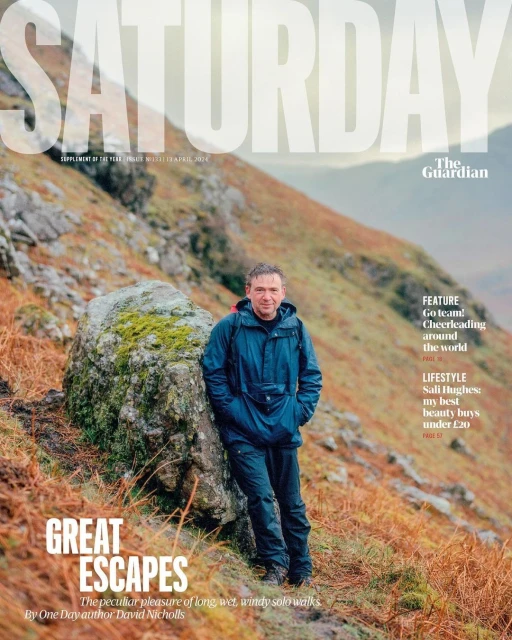 Magazine cover featuring a man in outdoor gear standing near a mossy boulder on a mountain hillside, with the text 'SATURDAY' and 'GREAT ESCAPES'.