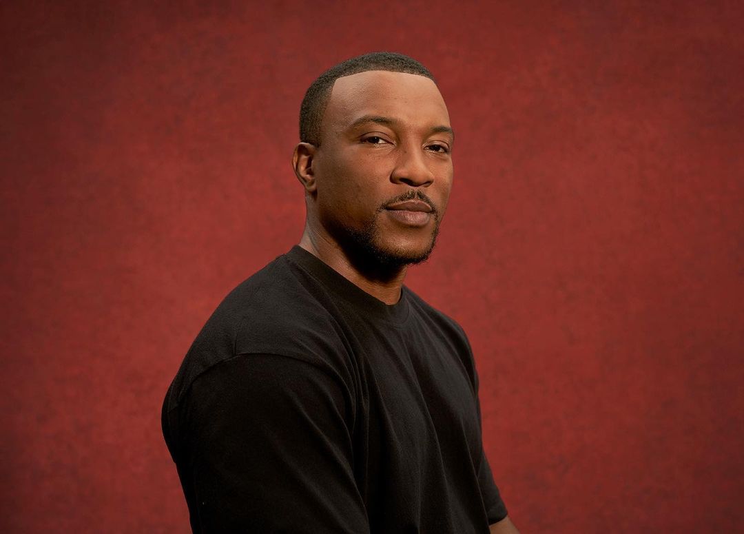 Portrait of a black man wearing a black t-shirt against a textured dark red background