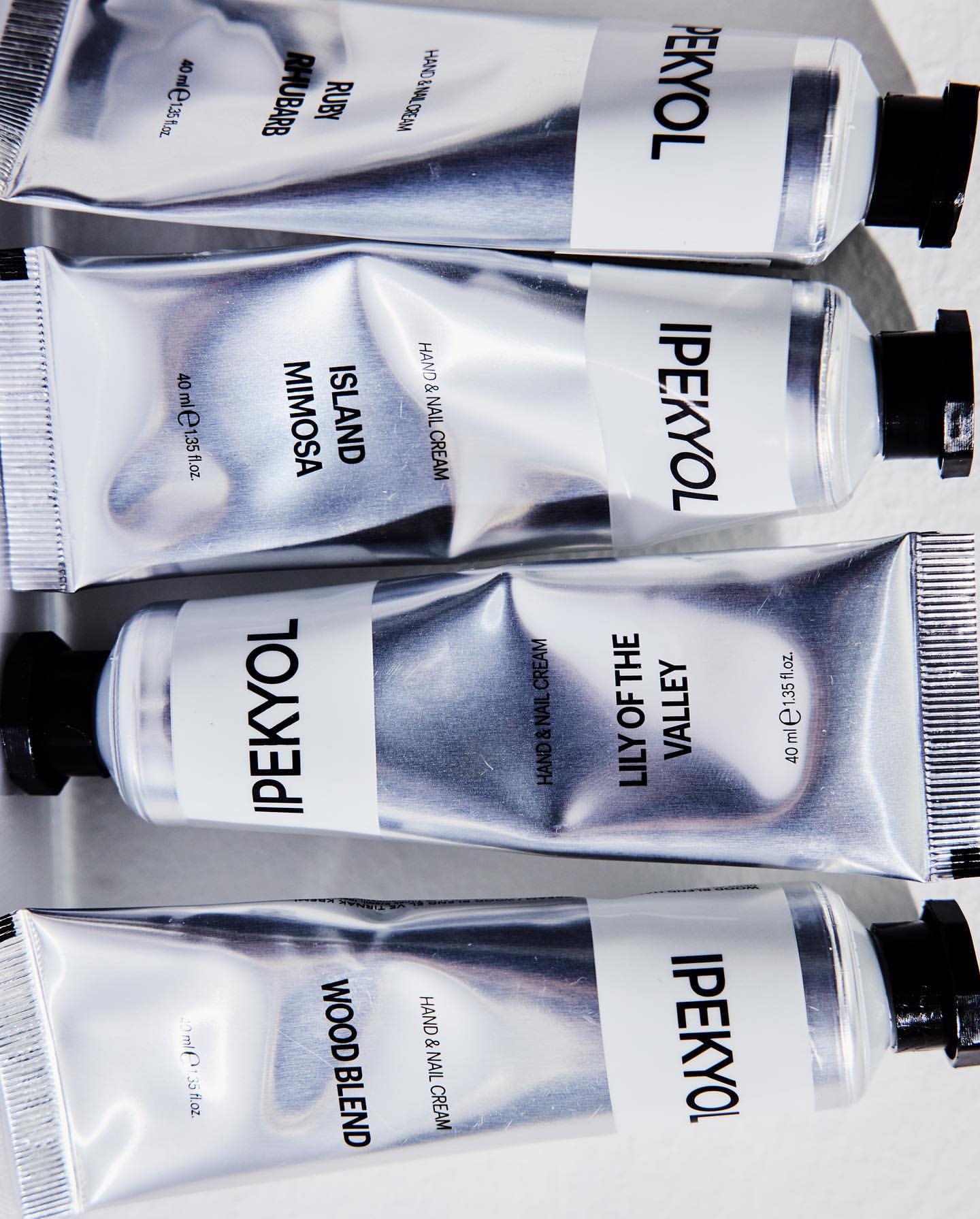 Four silver IPEKYOL hand cream tubes in a flat lay. Each tube features different scent names: Ruby Rhubarb, Island Mimosa, Lily of the Valley, Wood Blend.