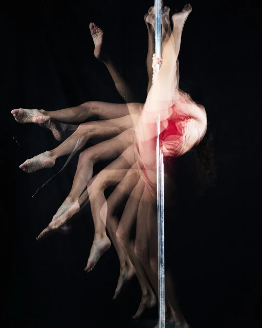 Woman performing pole dance, captured in multiple exposures on a chrome pole against a black background, showcasing movement and athleticism.