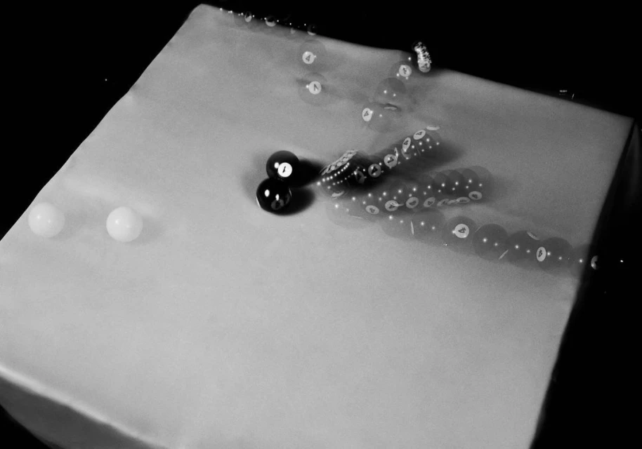 Monochrome image of two pool balls resting on a pool table, with motion blur showing the trajectory of another ball.