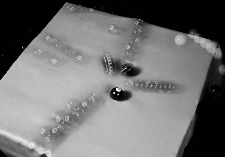 Monochrome image features pool balls in motion, captured using long exposure, showcasing a central '8' ball surrounded by blurred trails.
