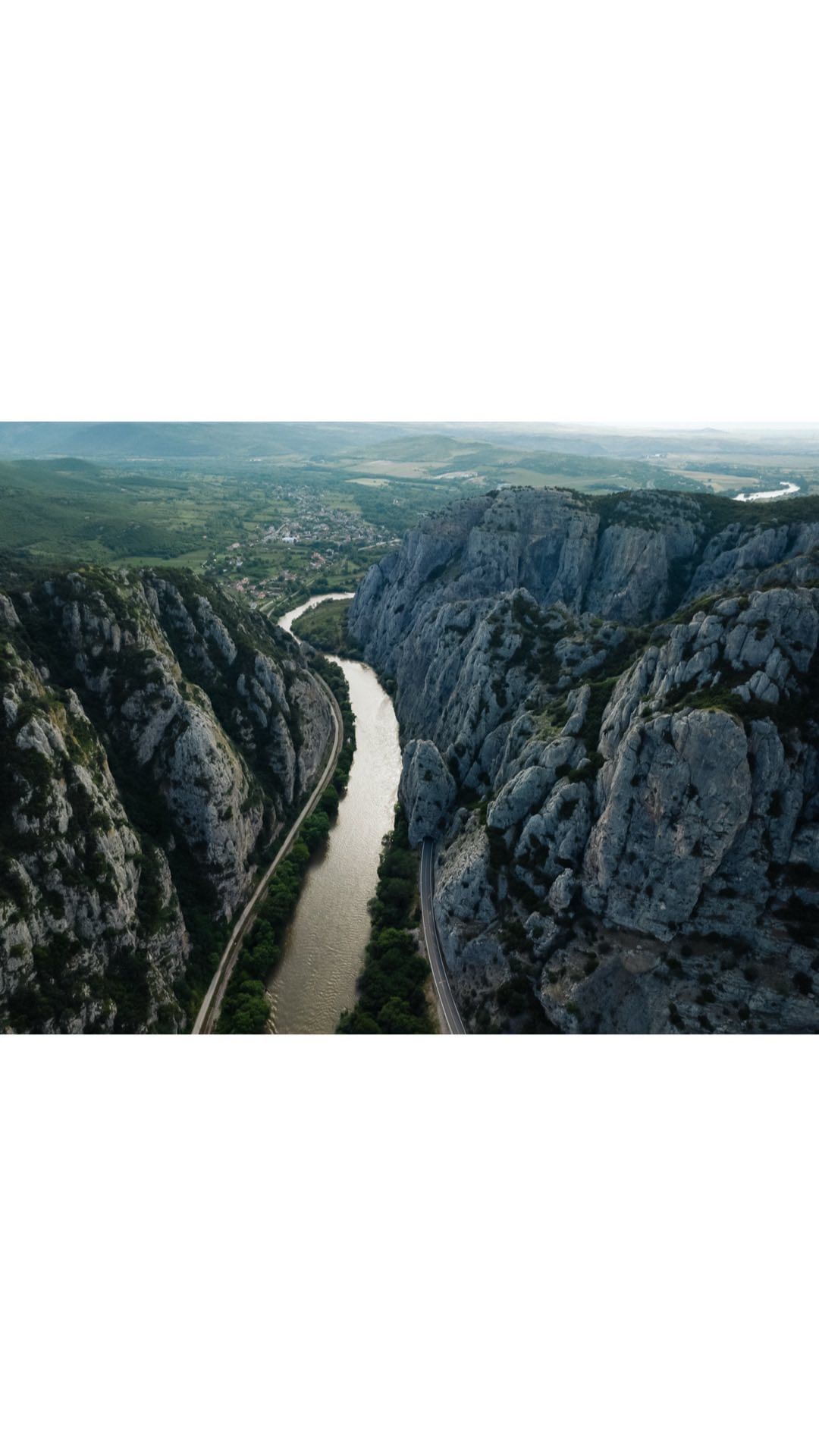 High-angle landscape shot of a river cutting through a canyon surrounded by rock formations and lush greenery on a sunny day.