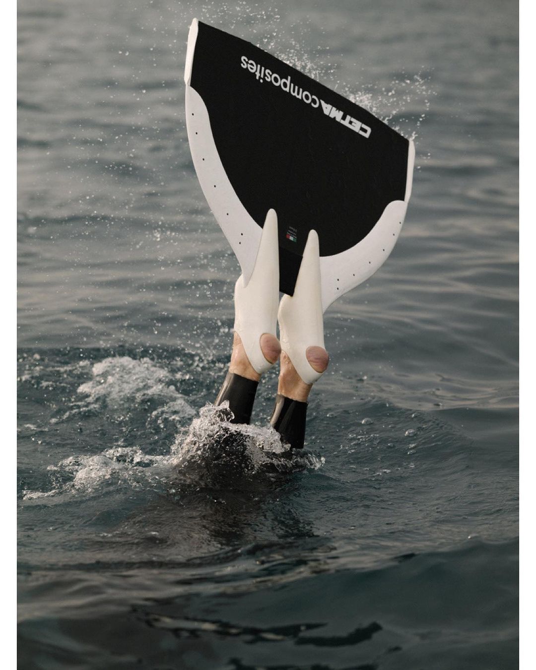 Underwater diver's legs and feet wearing fins emerging from ocean water, showcasing CETMA Composites freediving gear.