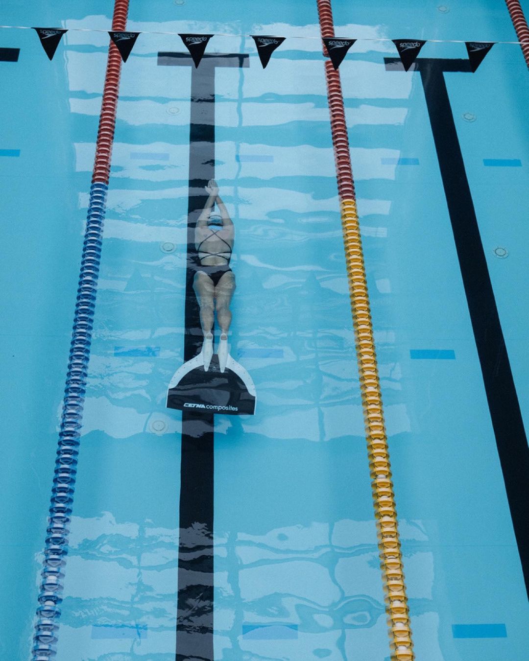 Overhead view of a swimmer with a monofin in an outdoor pool, divided by lane markers with clear blue water.
